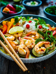 Tom Kha - Thai soup with prawns and rice noodles on wooden table
