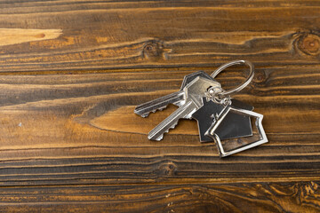 Keys from the house with a keychain in the form of a house. Composition on brown texture wood. Design element. Real estate and insurance concept. Copy space.