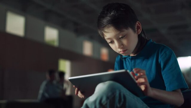 Focused boy surfing internet using pad computer closeup. Teen pupil sitting hall