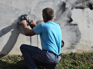 Wall cleaning with an angle grinder. Graffiti removal. City vandals. Removal of paint from concrete surfaces
 - obrazy, fototapety, plakaty