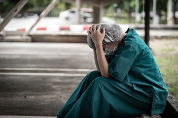 Naklejka premium Tired depressed female asian scrub nurse wears face mask blue uniform sits on hospital floor,Young woman doctor stressed from hard work