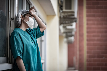 Tired depressed female asian scrub nurse wears face mask blue uniform sits on hospital floor,Young woman doctor stressed from hard work