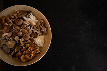 Bowl on left with a mixture of wild mushrooms in bamboo bowl on black background.