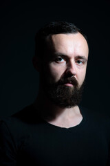 Obraz premium dramatic portrait of bearded millennial on black background
