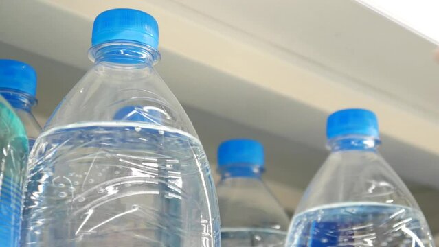 Close-up of plastic bottles with carbonated water on a store shelf and a male buyer takes one