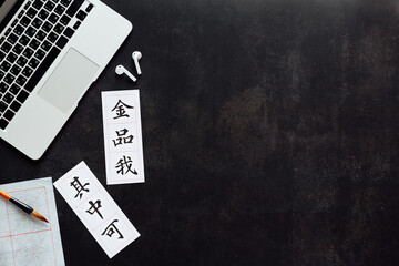 Flat lay mockup for online courses of Chinese language. Laptop and cards with basic printed characters on dark black concrete background with copy space. Inscription: that, middle, can, gold, taste, i