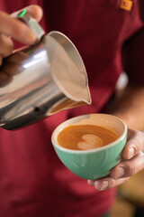 barista in a red t-shirt pours coffee into a green cup