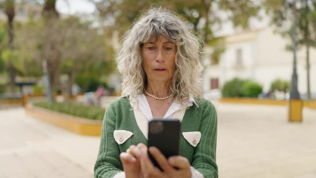 Middle age woman smiling confident using smartphone at park