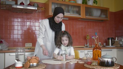 Muslim family spend time in the kitchen. Mom and daughter cut out dough circles with a glass. Cooking dumplings