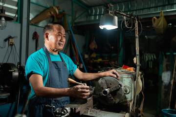 Portrait of Asian senior man working as a steel lathe is preparing work and equipment to turn steel and a small lathe in the family industry..