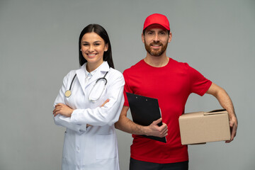 Happy male courier in red uniform with cardboard parcel and female confident doctor looking at the...