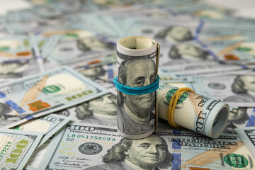 Money, a roll of US one hundred dollar bills on a background of scattered banknotes on a black texture. Money is scattered on the table. Concepts of finance and economics. Money accumulation concept. 