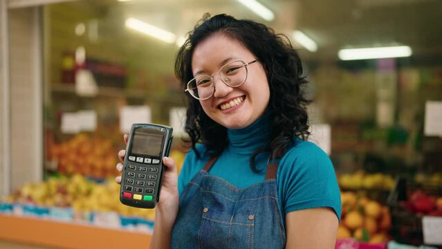 Young chinese woman employee smiling confident holding data phone at fruit store
