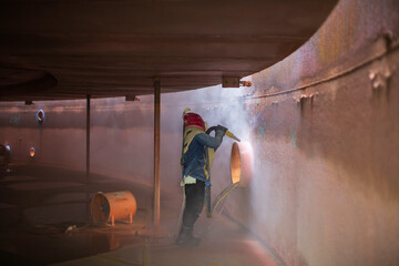 Male worker surface corrosion plate preparation by sand blasting of tank internal oil