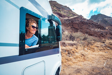 Happy adult woman smile and enjoy travel destination inside her camper van. Cheerful female people...