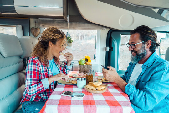 Man and woman have lunch together inside a modern camper van rv vehicle in renting holiday vacation. Happy adult couple enjoy off grid van life lifestyle. People in indoor leisure activity