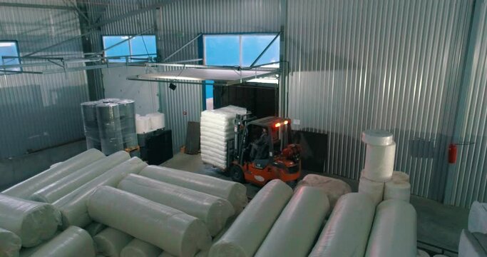 A forklift in a warehouse moves white bags. A forklift works in a warehouse. Forklift transports goods. White bags in a factory warehouse