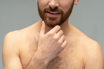 Obraz premium Cropped portrait view of a young handsome naked man posing after taking a shower over the grey wall background. Stock photo
