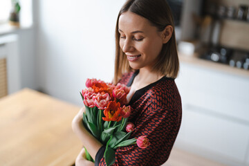 Happy woman enjoy bouquet of tulips. Housewife enjoying a bunch of flowers and interior of kitchen. Sweet home. Allergy free