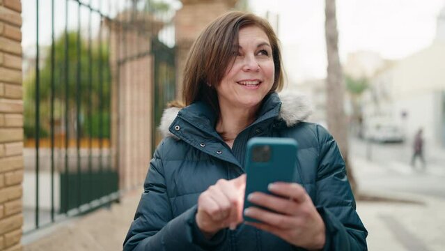 Middle age woman smiling confident using smartphone at street