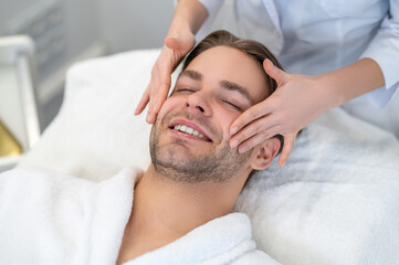 Obraz na płótnie Canvas Young man having face massage in a beauty salon
