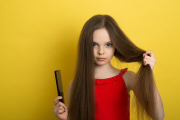 Cute little baby shows off her long healthy hair with a comb in her hand. The concept of a baby and healthy hair. A little girl is trying to comb her hair. Hairstyles.