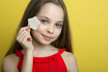 Pretty kid cleansing her face by heart shape cotton pad. Portrait of beautiful little girl enjoying skincare procedures