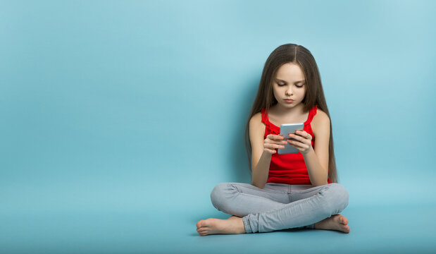 Cute little child with long healthy hair with smartphone in hand sits in the studio. Kid with gadgets concept. Little girl with new technologies
