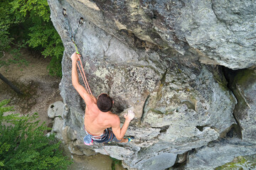 Young man climbing steep wall of rocky mountain. Male climber overcomes challenging route. Engaging...