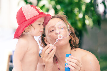 Fun summer day with family. Happy child blowing bubbles. Mom and daughter by the pool. Little girl plays with soap bubbles