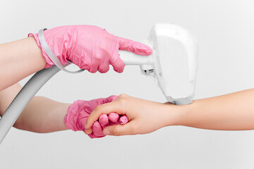 Laser hair removal on the hand on a white background. Pink gloves hold the epilation device on a...