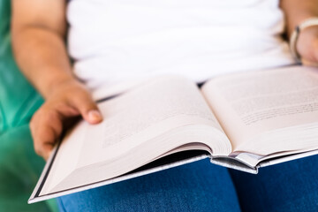 Closeup a woman is sitting on the chair and reading a book that rest on her lap, focus at the book