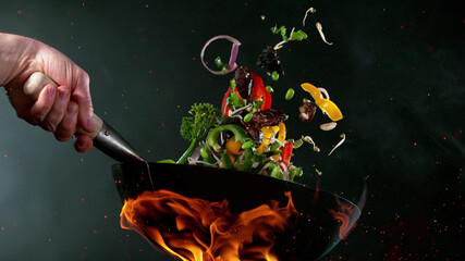 Closeup of chef throwing vegetable mix from wok pan in fire.