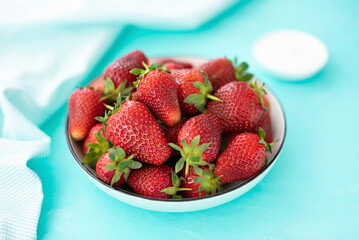 large ripe freshly picked strawberries in a ceramic plate on a turquoise background