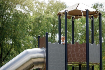 A little boy in the high observation tower of the playground prepares to slide through a metal...