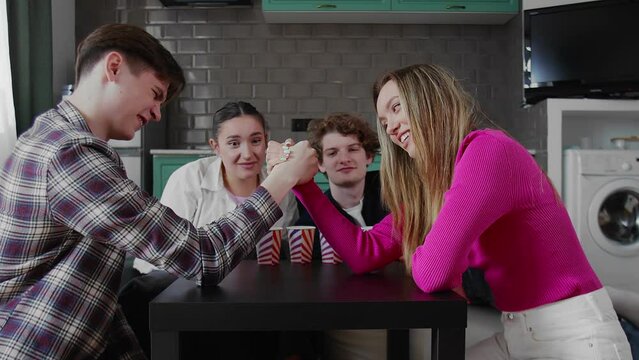 A group of friends are playing arm wrestling. Boy and girl wrestle on the table