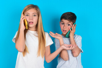 two kids boy and girl standing over blue studio background talking on the phone stressed with hand...