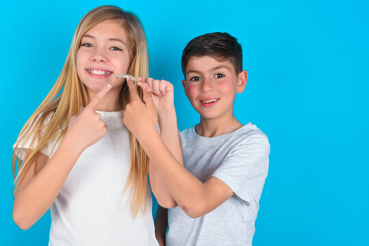 two kids boy and girl standing over blue studio background holding an invisible aligner and pointing at it. Dental healthcare and confidence concept.