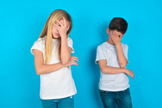 two kids boy and girl standing over blue studio background making facepalm gesture while smiling amazed with stupid situation.