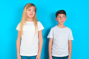 two kids boy and girl standing over blue studio background, looks pensively aside, plans actions after university, imagines what to do Thinks over about new project.