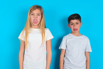 Body language. Disgusted stressed out two kids boy and girl standing over blue studio background, frowning face, demonstrating aversion to something.