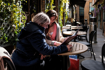 Portrait of two multiracial mature friends women having a coffee in a terrace in London.