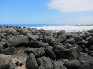 Black volcanic rocks against a deep blue sea. Waves, blue sky and white clouds. Rocky beach at Lehia Park, Hilo, Big Island of Hawaii.