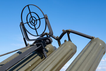 The gun sight and barrels of a old anti-aircraft gun are looking on the blue cloudless sky