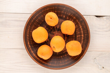 Several juicy sweet apricots with a ceramic plate on a wooden table, close-up, top view.