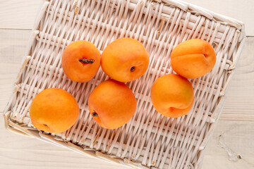 Several juicy sweet apricots with a vine mat on a wooden table, close-up, top view.