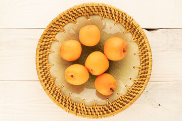 Several juicy sweet apricots with a ceramic plate on a wooden table, close-up, top view.