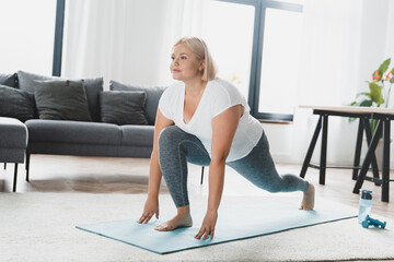 Fototapeta na wymiar Home fitness concept. Plump plus size woman athlete training workout practicing yoga on fitness mat, stretching her legs, burning calories weight