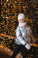 Girl and Christmas lights. Smiling little girl in a bright hat, scarf and jacket at night with blurry lights. Holidays theme