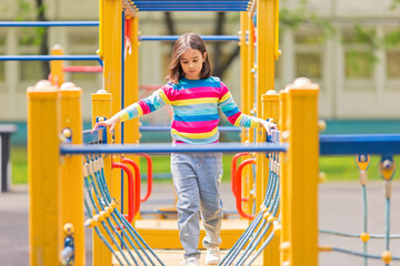 little cute girl 5-6 years old on a childrens ladder on a bright yellow playground